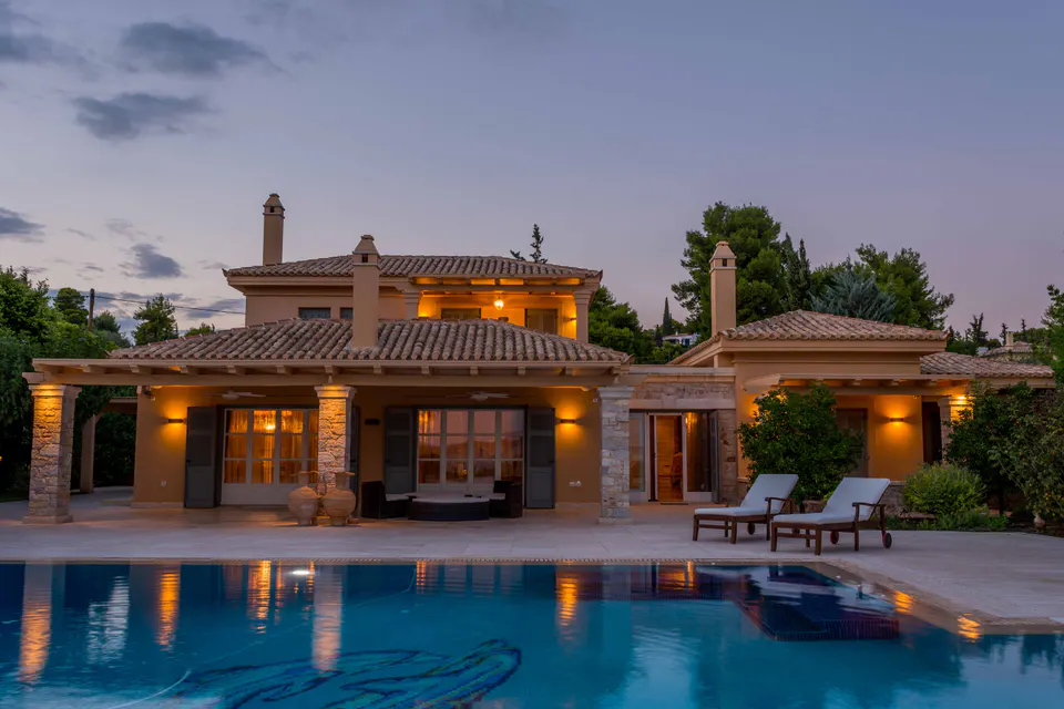 The villa and its pool at dusk, with the lights on