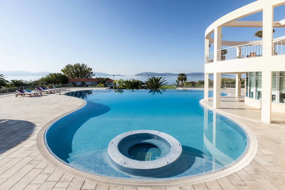 Curved swimming pool with a round hot tub, sun loungers and the sea beyond
