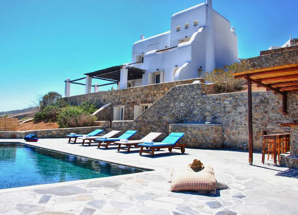 White villa behind the pool, with sun beds and a stone terrace