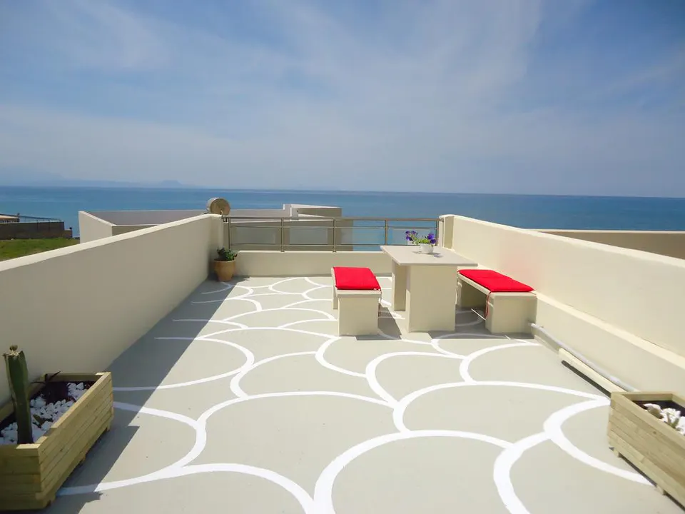 Roof terrace with a table, two benches with red cushions and a view of the sea