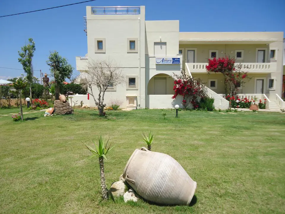 Apartment building with red flowering bushes and a large clay jar on the lawn