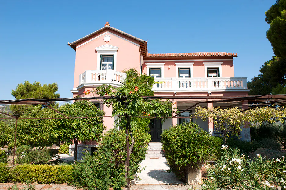 The pink villa seen from the garden, with a pergola and trees in front