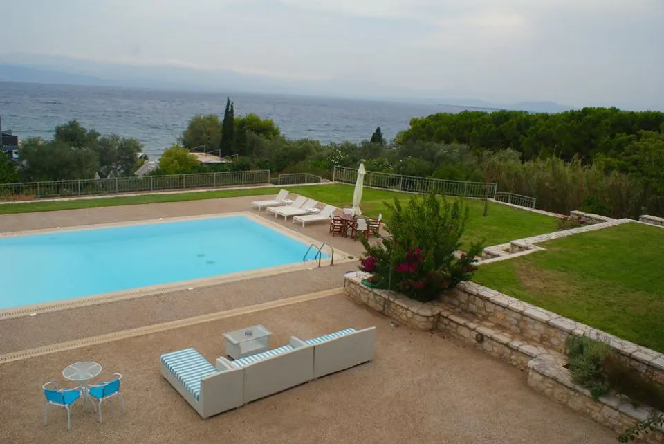 Pool, lawn and sofas seen from above, with the sea beyond