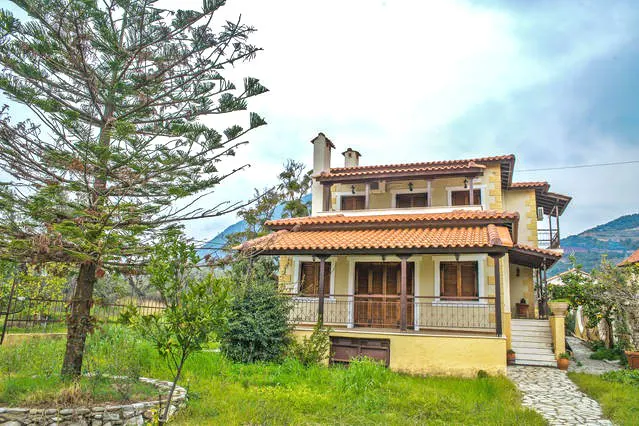 The villa seen from the garden, with a tiled roof, balconies and a tall conifer on the left