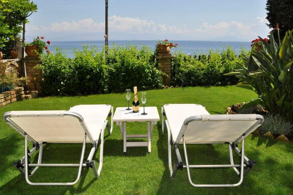 Two sun loungers and a small table on the lawn, the sea beyond